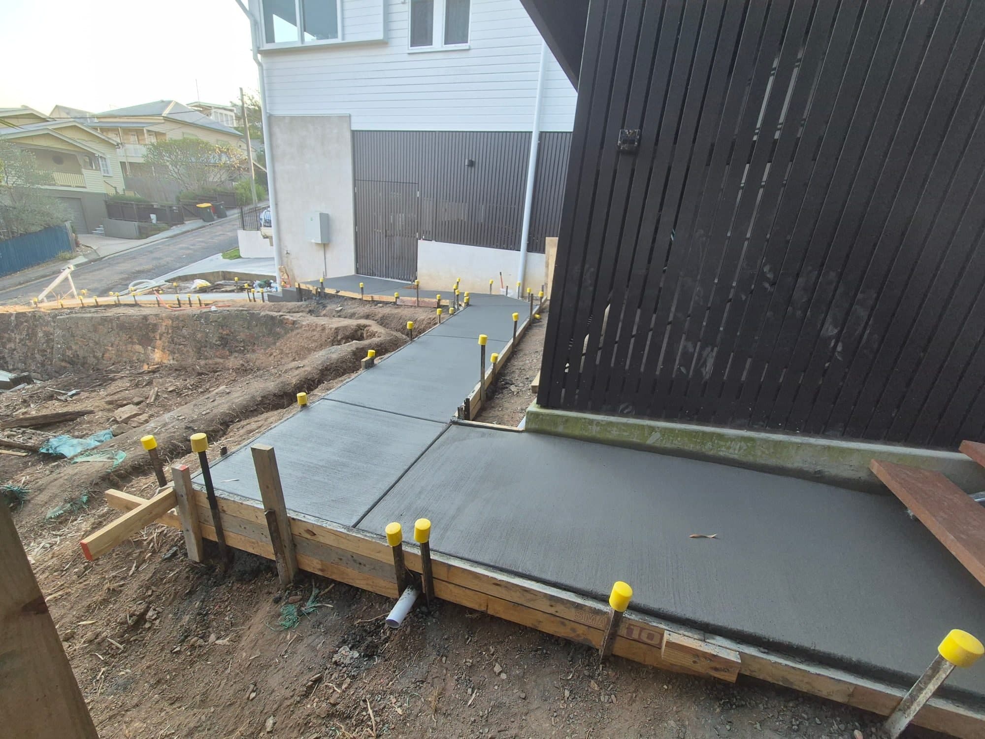Freshly poured concrete path beside a home, formwork still in place